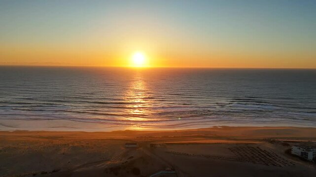 Aerial drone view of golden sunset reflecting on ocean waves and sandy beach, capturing peaceful coastal light and natural beauty at dusk in a serene and scenic seascape moment.
