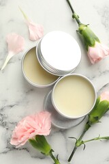 Moisturizing lip balms and pink flowers on white marble table, flat lay