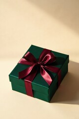 A luxuriously wrapped emerald green gift box adorned with a rich burgundy satin ribbon bow, displayed against a soft beige backdrop under gentle sunlight.