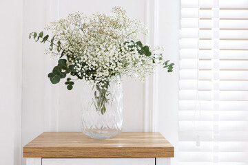 Beautiful gypsophila flowers and eucalyptus branches in vase on table at home. Space for text