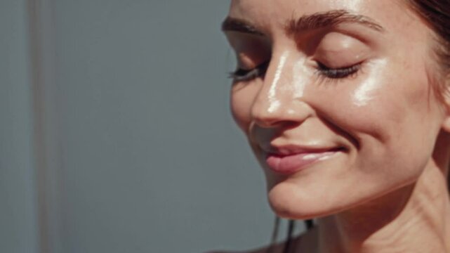  cinematic close-up portrait of a woman smiling with her eyes closed, basking in bright natural sunlight. Her skin glows with a healthy, dewy sheen, and fine highlights shimmer along her cheekbones 