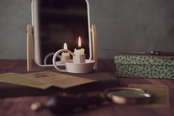 Lit candle in front of a mirror on a table with a box, letter opener and magnifying glass