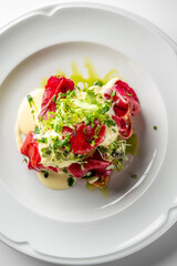 A gourmet dish featuring a toasted base topped with thinly sliced cured meat, greens, and a rich, creamy sauce drizzled over. Perfect for food enthusiasts.