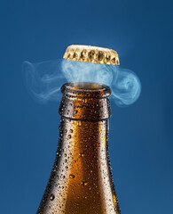 Opening chilled beer bottle on blue background. Gas impurring from the beer bottle and blows cap...