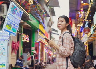 Young woman exploring vibrant alley filled with festive lights and decorations in a bustling Asian city during evening hours