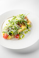 A beautifully plated omelette filled with fresh greens, tomatoes, and sliced meat, drizzled with herb sauce on a white background.