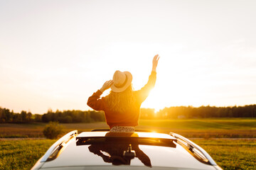Beautiful woman with curly hair feels freedom from car window against sunset background. Young...