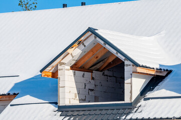 A dormer is being framed on a snow-covered roof, with the block work and wooden beams visible.