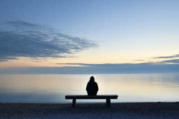 Obraz premium Person sits peacefully on a bench at the beach, gazing at the calm ocean during a tranquil twilight hour