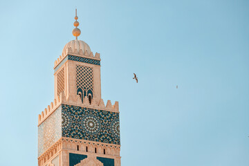 Sunlight illuminating intricate details of the Hassan II Mosque minaret against a clear sky,...