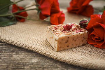 Handmade rose soap bar with dried petals on top, placed on burlap with fresh red roses. Natural...