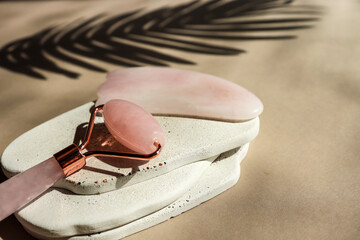 Close-up of a rose quartz facial roller and gua sha tool on a modern ceramic tray with wave...