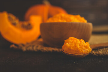 Closeup of mashed pumpkin on a wooden spoon with a rustic bowl and fresh pumpkin slices in the...