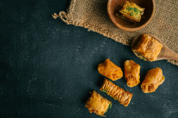 Freshly baked baklava pieces on a dark surface with a wooden spoon, showcasing flaky layers and nutty filling, ideal for dessert photography.