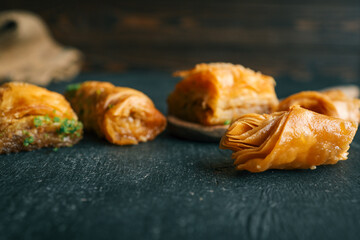 Close-up of traditional baklava pieces with layered golden pastry and syrup on dark rustic background. Sweet dessert with flaky texture and pistachio crumbs