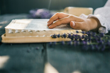 Child’s hands reading the Bible at a rustic table with a bundle of lavender and a cup of tea in the background. Peaceful morning devotion in natural light
