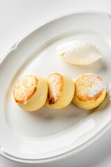Three golden-brown cheese pancakes on a white plate, accompanied by a scoop of creamy white cheese, creating an appetizing and inviting presentation.