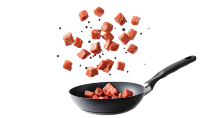 Diced meat cubes falling into a frying pan with a black background and a gray handle visible too