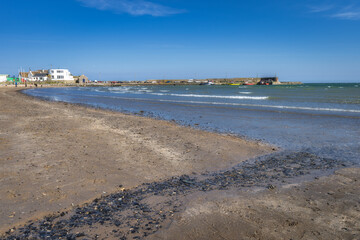 A picturesque beach and pier scene showcases gentle waves lapping at the pebbled shoreline beneath a clear blue sky, creating a perfect coastal paradise by the sea, Loughshinny, Dublin, Ireland