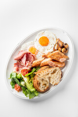 A delectable breakfast plate featuring crispy bacon, sunny-side-up eggs, sautéed mushrooms, fresh salad, and toasted bread, served on a white oval dish.