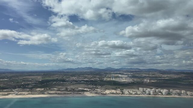 An immersive view through the pilot&rsquo;s eyes from inside a jet cockpitm in a real time approach to Alicante airport, flying over the Mediterranean Sea, under a blue sky with some fluffy clouds.