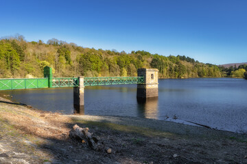 This scene depicts a tranquil lake with a green walkway and a weathered tower, surrounded by vibrant trees under a clear blue sky, ideal for relaxation, Bohernabreena Reservoir, Dublin, Ireland