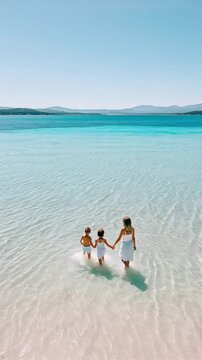 Mother and children walking through the water on a paradise beach
