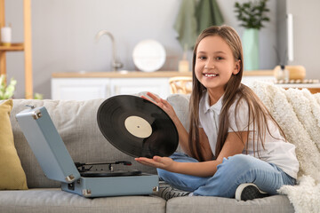 Little girl with vinyl disc and record player sitting on sofa at home