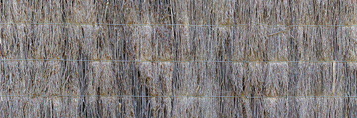 Fototapeta premium Natural brushwood fence banner made from tightly packed twigs and sticks, bound with horizontal wire. Rustic, organic, abstract texture with earthy tones and a dense, woven pattern.