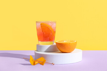 Podiums with glass of tasty Negroni cocktail and orange on color background