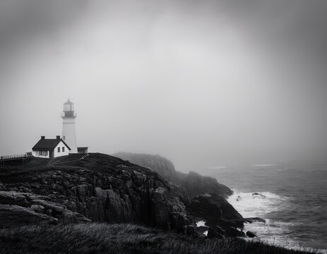 lonely lighthouse on dramatic foggy cliff black and white minimalist photography of coastal landscape with moody atmosphere and ocean views