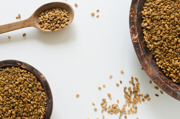 Dry fenugreek or shambhala in bowls and spoon on white wooden table. Medicinal plant from the Middle East. Alternative medicine concept. Selective focus. Copy space. Horizontal orientation