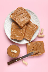 Plate of toasts with peanut butter and nuts on pink background