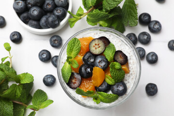Delicious chia pudding with blueberries, peaches and mint in glass on white table, flat lay