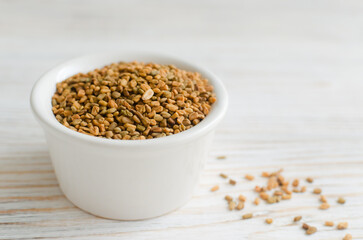 Dry fenugreek or shambhala in a bowl on a white wooden table. Medicinal plant from the Middle East. Alternative medicine concept. Selective focus. Copy space. Horizontal orientation