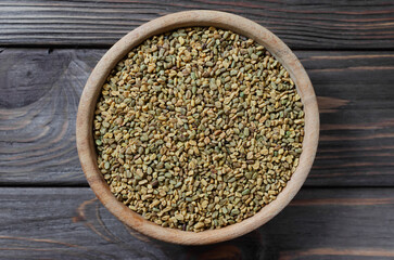 Dry fenugreek or shambhala in a wooden bowl on a black table. Medicinal plant from the Middle East. Alternative medicine concept. Top view. Selective focus.
