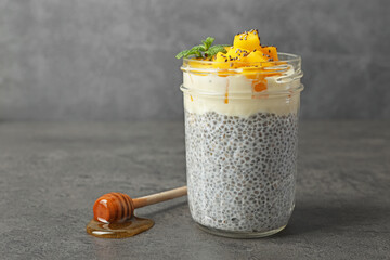 Delicious chia pudding with mango and mint in glass on gray textured table, space for text