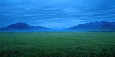 Fototapeta premium Vast green grassland under a deep blue twilight sky. Layered mountain silhouettes on a wide horizon. Calm resilience and future possibility. Ideal for travel, wellness, and brand storytelling.