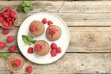 Delicious muffins with raspberries and mint on wooden table, flat lay. Space for text