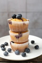 Stack of delicious muffins with blueberries on wooden table against grey tiled background, closeup