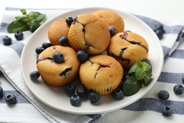 Delicious muffins with blueberries and mint on white table, closeup