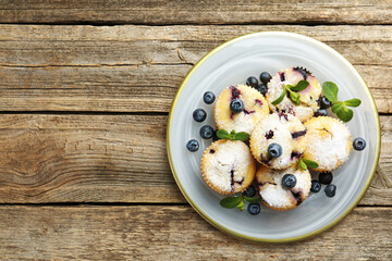 Delicious muffins with blueberries, powdered sugar and mint on wooden table, top view. Space for text