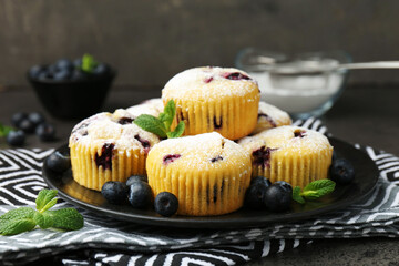 Delicious muffins with blueberries, powdered sugar and mint on dark table, closeup