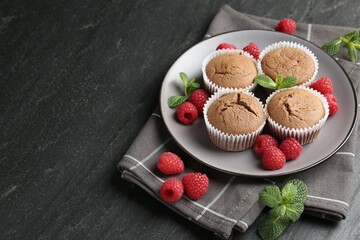 Delicious muffins with raspberries and mint on dark textured table, closeup. Space for text