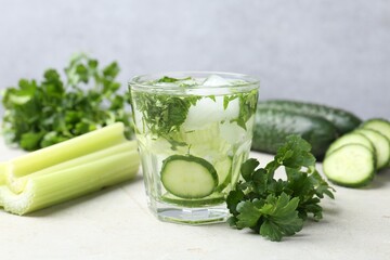 Healthy drink with parsley, cucumbers and celery on light table, closeup