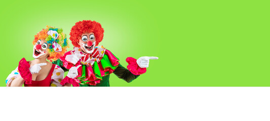 Female clown and male clown pointing at blank template copy spase for advertising, posters, greetings, invitations. Entertainer as Joker in a suit and wig, with clown whiteface makeup.