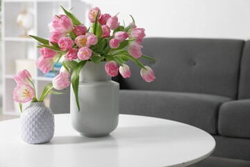 Beautiful tulips in vases on table indoors. Space for text