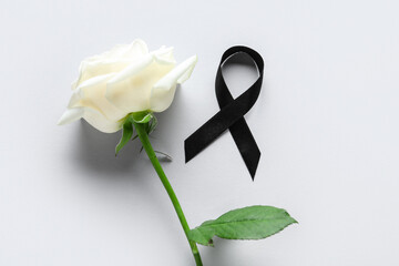 Beautiful rose flower and black funeral ribbon on grey background