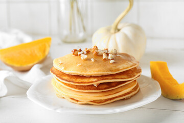Plate of tasty pumpkin pancakes with honey and nuts on white wooden table