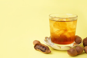 Glass of tasty tamarind drink and fruits on yellow background